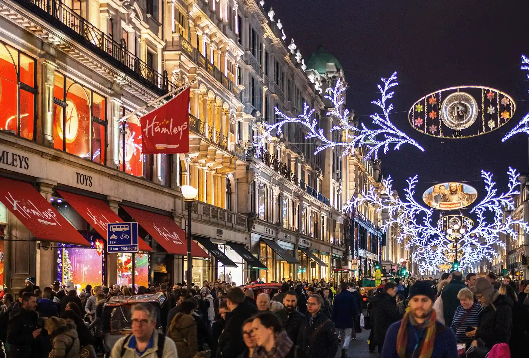 During the Christmas season, shoppers stroll along Regent Street in London, passing Hamleys toy store and other decorated storefronts. Regent Street in London during Christmas is lined with decorated storefronts, including Hamleys.