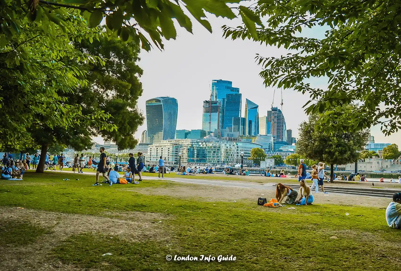 People relaxing and walking past Potters Fields Park while admiring the view of the City of London London England. A view of The City of London from Potters Fields Park.