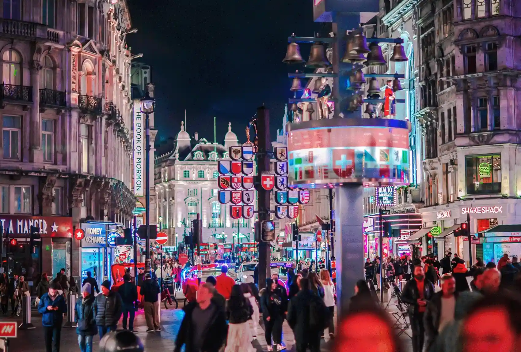 At night, Leicester Square, London, is illuminated by festive lights and crowded with people shopping. London's Leicester Square at night with festive lights and people shopping.