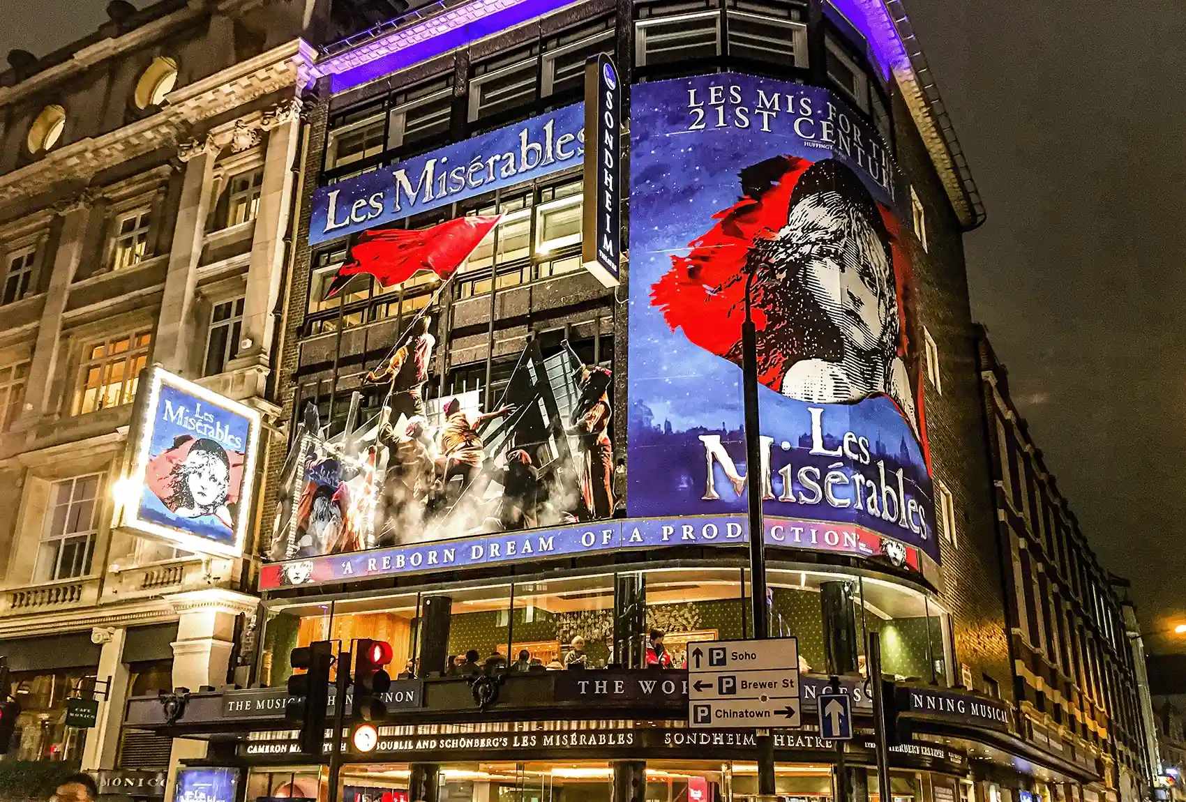 Sondheim Theatre in London illuminated with 'Les Misérables' posters at night.