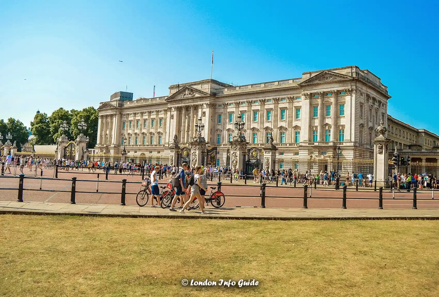 People walking on the exterior of Buckingham Palace, close to the main entrance gate. Buckingham Palace in London on a beautiful sunny summer day.