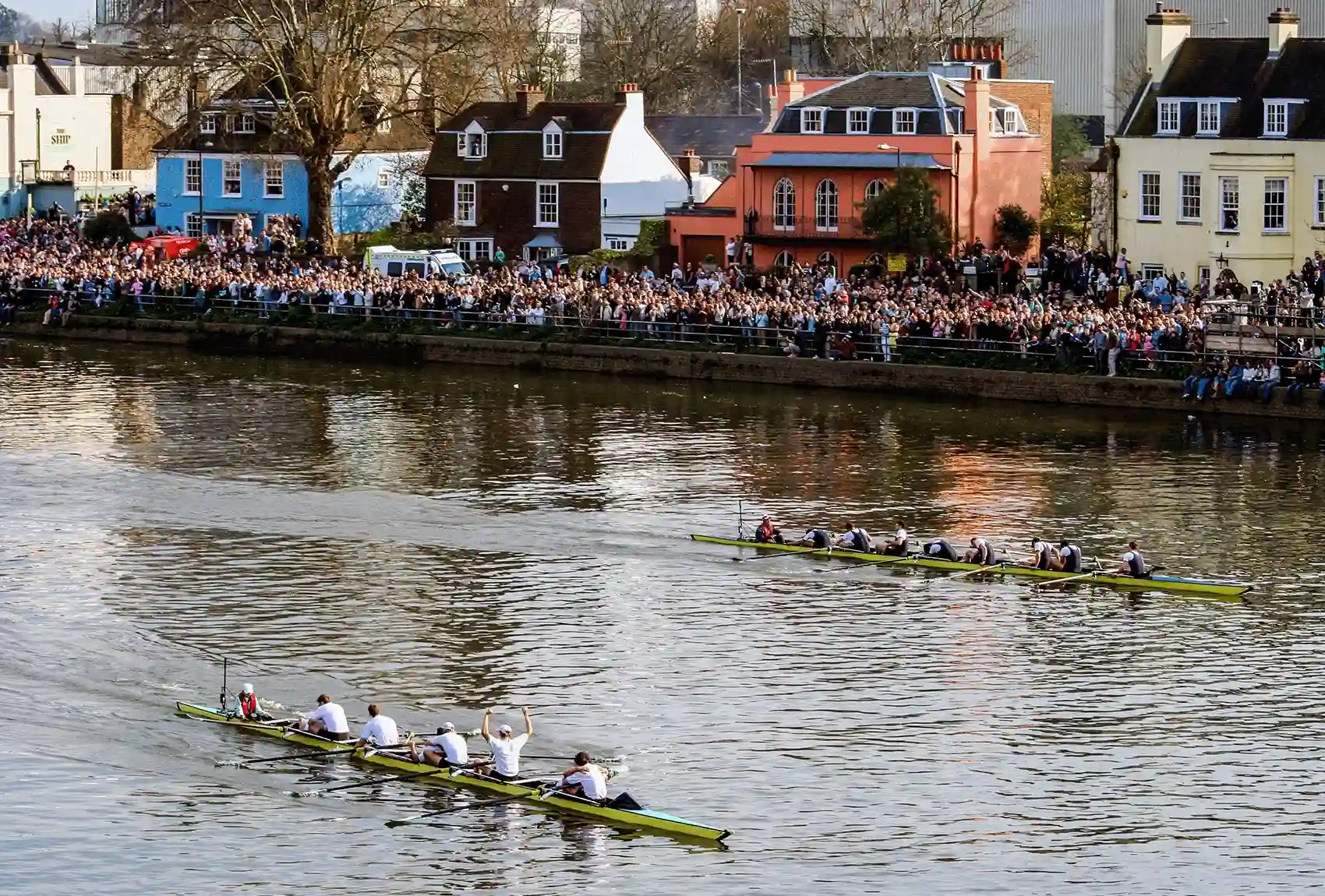 Oxford and Cambridge crews racing past crowds on Thames river.