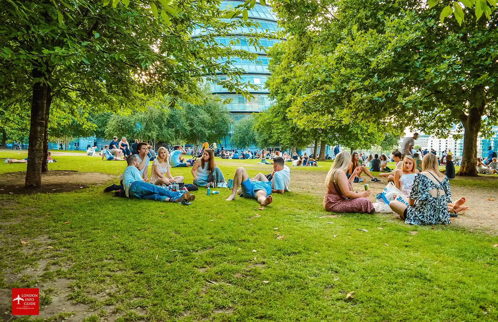 Groups of people sitting and chatting on the grass. Is London worth visiting? People relaxing on green spaces London.