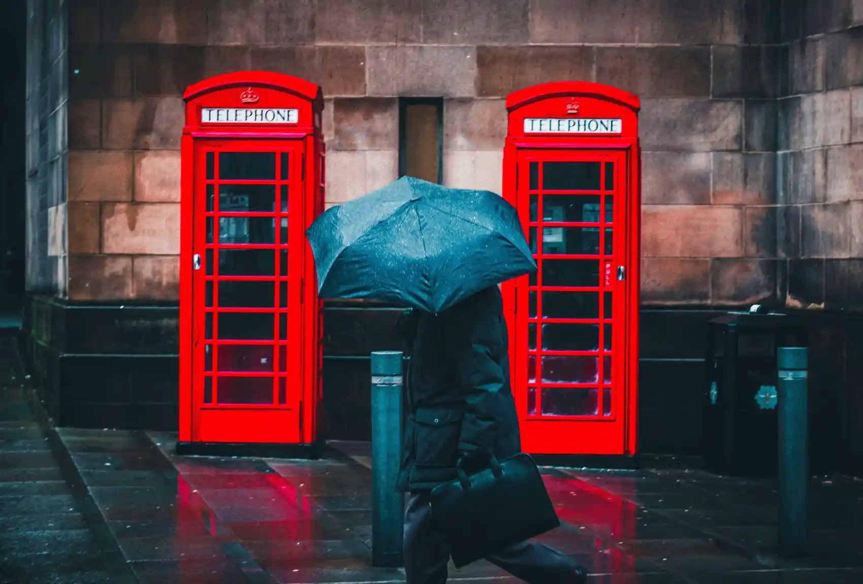 London’s red phone booths in the rain with a person walking by. Red telephone booths on a regular rainy day in London.