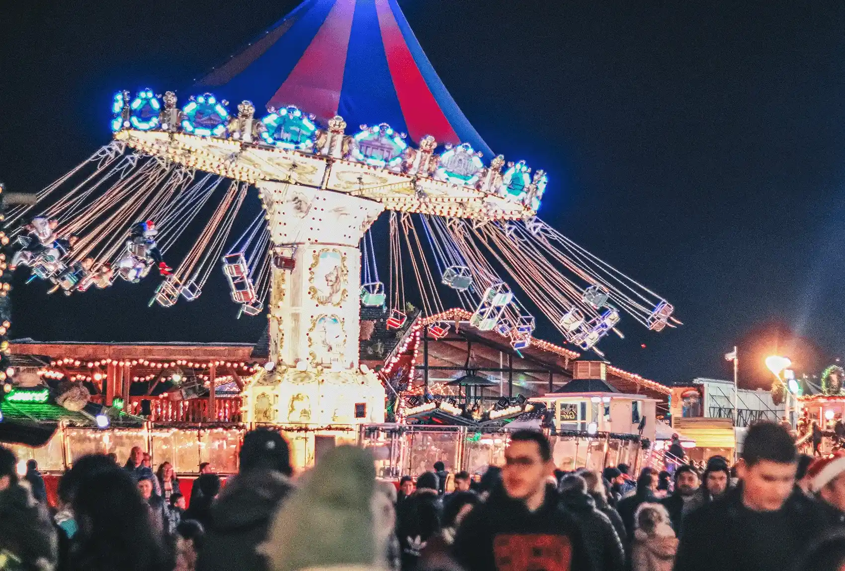 A lively evening scene at Winter Wonderland, Hyde Park, London, with crowds enjoying the various activities against the night sky. A festive fairground swing ride at Winter Wonderland, Hyde Park.